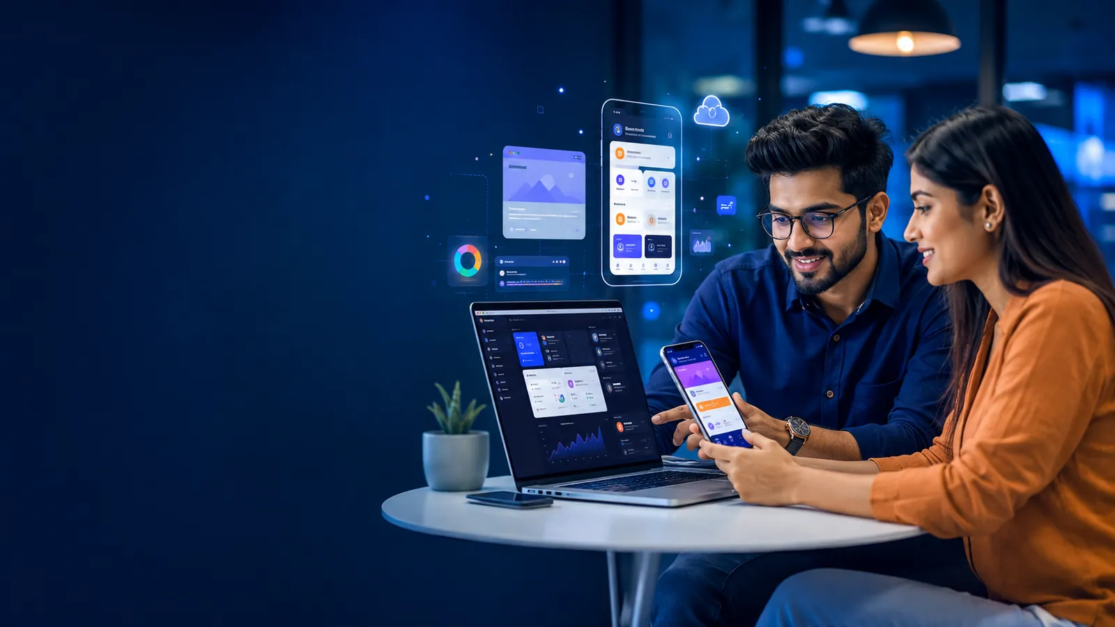 An Indian software developer and a business owner reviewing a mobile app dashboard on a laptop and smartphone